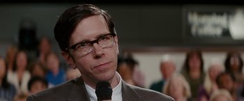 Movie still from “Confessions of a Shopaholic” (2009), directed by P.J. Hogan – A man with glasses is holding a microphone in his hand; Close Up shot, Over the shoulder angle