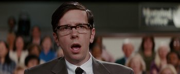 Movie still from “Confessions of a Shopaholic” (2009), directed by P.J. Hogan – A man in a suit and glasses looking surprised; Close Up shot, Over the shoulder angle