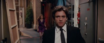 Movie still from “Confessions of a Shopaholic” (2009), directed by P.J. Hogan – A man in a suit and tie standing next to a woman in a purple dress; Medium shot, Over the shoulder angle