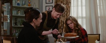 Movie still from “Confessions of a Shopaholic” (2009), directed by P.J. Hogan – A woman cutting a cake with two women looking on; Medium shot, Over the shoulder angle