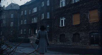 Movie still from “Confidence” (1980), directed by István Szabó – A woman is walking down the street in front of a brick building; Extreme Wide shot, Low angle
