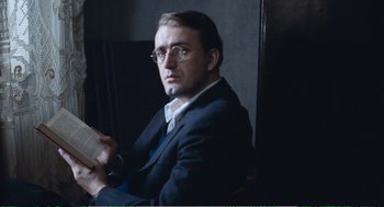 Movie still from “Confidence” (1980), directed by István Szabó – A man sitting in a chair holding an open book; Close Up shot, Low angle