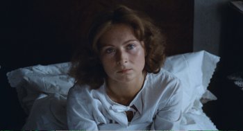 Movie still from “Confidence” (1980), directed by István Szabó – A woman sitting on top of a bed in a white shirt; Close Up shot, High angle