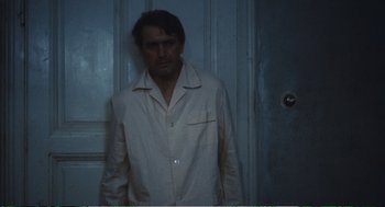 Movie still from “Confidence” (1980), directed by István Szabó – A man standing in front of a door wearing pajamas; Medium shot, Low angle