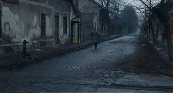 Movie still from “Confidence” (1980), directed by István Szabó – A person walking down a street near a building; Extreme Wide shot, High angle