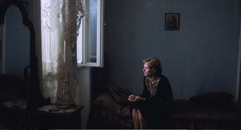 Movie still from “Confidence” (1980), directed by István Szabó – A woman sitting on a couch looking out of a window; Medium shot, Over the shoulder angle