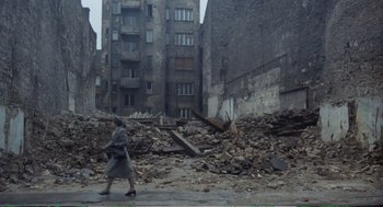 Movie still from “Confidence” (1980), directed by István Szabó – A woman walking down a street past a pile of rubble; Extreme Wide shot, High angle