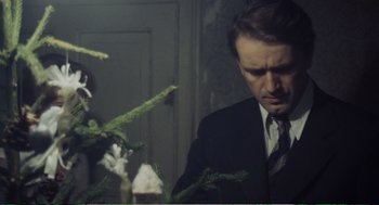 Movie still from “Confidence” (1980), directed by István Szabó – A man standing next to a plant in a dark room; Close Up shot, Low angle