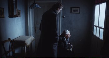 Movie still from “Confidence” (1980), directed by István Szabó – A man standing next to another man sitting in a chair; Wide shot, High angle