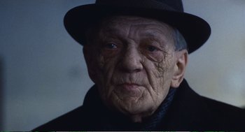 Movie still from “Confidence” (1980), directed by István Szabó – An old man wearing a black hat and a black coat; Close Up shot, Low angle