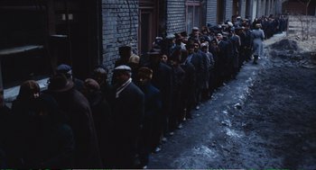 Movie still from “Confidence” (1980), directed by István Szabó – A group of people standing in a long line outside of a building; Wide shot, High angle