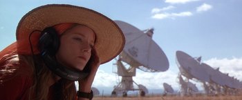 Movie still from “Contact” (1997), directed by Robert Zemeckis – A woman in a straw hat talking on a cell phone in front of a satellite dish; Close Up shot, Low angle