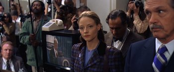 Movie still from “Contact” (1997), directed by Robert Zemeckis – A woman in a plaid jacket standing in front of a tv; Close Up shot, Over the shoulder angle