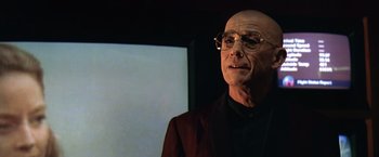 Movie still from “Contact” (1997), directed by Robert Zemeckis – A bald man wearing glasses and a jacket; Close Up shot, Low angle