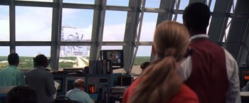 Movie still from “Contact” (1997), directed by Robert Zemeckis – A woman watches television in an airport terminal; Extreme Wide shot, Over the shoulder angle