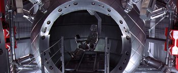 Movie still from “Contact” (1997), directed by Robert Zemeckis – A man sitting in a chair in a room with a computer; Wide shot, Overhead angle