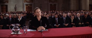 Movie still from “Contact” (1997), directed by Robert Zemeckis – A woman sitting in front of a microphone in front of a group of people; Medium shot, Low angle