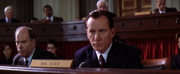 Movie still from “Contact” (1997), directed by Robert Zemeckis – A man in a suit and tie sitting in a courtroom; Close Up shot, Low angle