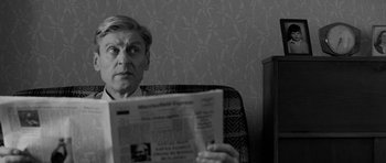 Movie still from “Control” (2007), directed by Anton Corbijn – A man sitting in a chair while reading a newspaper; Close Up shot, Over the shoulder angle