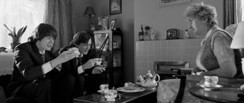 Movie still from “Control” (2007), directed by Anton Corbijn – A person sitting at a table with a cup of tea; Medium shot, Over the shoulder angle