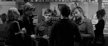 Movie still from “Control” (2007), directed by Anton Corbijn – A group of young men standing around a bar; Medium shot, Over the shoulder angle