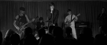 Movie still from “Control” (2007), directed by Anton Corbijn – A group of young men singing and playing instruments in front of an audience; Medium shot, Low angle