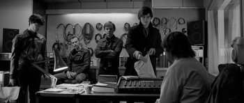 Movie still from “Control” (2007), directed by Anton Corbijn – A group of people sitting around a table; Medium shot, Over the shoulder angle