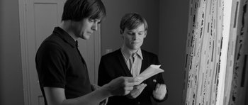 Movie still from “Control” (2007), directed by Anton Corbijn – Two young men are looking at a piece of paper; Medium shot, Over the shoulder angle