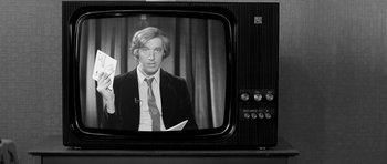 Movie still from “Control” (2007), directed by Anton Corbijn – A black and white photo of a man on a tv screen; Close Up shot, Over the shoulder angle