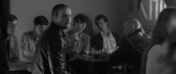 Movie still from “Control” (2007), directed by Anton Corbijn – A group of men sitting around a table with drinks; Medium shot, Over the shoulder angle