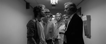 Movie still from “Control” (2007), directed by Anton Corbijn – A black and white photo of a group of men standing in a hallway; Medium shot, Low angle