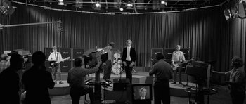 Movie still from “Control” (2007), directed by Anton Corbijn – A black - and - white photo of a man in a suit on a stage; Wide shot, High angle