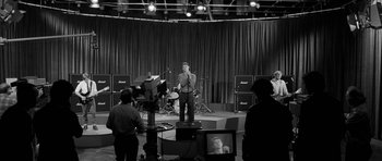 Movie still from “Control” (2007), directed by Anton Corbijn – A black and white photo of a man singing; Wide shot, High angle