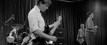Movie still from “Control” (2007), directed by Anton Corbijn – A young man playing an electric guitar in front of a group of speakers; Medium shot, Low angle