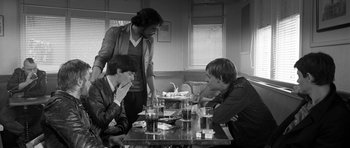 Movie still from “Control” (2007), directed by Anton Corbijn – A group of young men sitting at a table; Medium shot, Over the shoulder angle