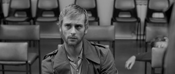 Movie still from “Control” (2007), directed by Anton Corbijn – Black and white photograph of a man in front of a row of seats; Close Up shot, Over the shoulder angle