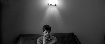 Movie still from “Control” (2007), directed by Anton Corbijn – A man sitting on top of a couch under a light; Close Up shot, Low angle