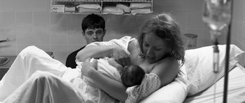 Movie still from “Control” (2007), directed by Anton Corbijn – A young man and a woman holding a newborn baby; Medium shot, Over the shoulder angle