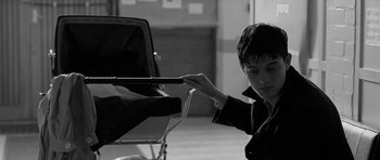 Movie still from “Control” (2007), directed by Anton Corbijn – A young man holding onto a rope while sitting in a chair; Medium shot, High angle