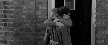 Movie still from “Control” (2007), directed by Anton Corbijn – A young boy and a young girl hugging each other; Medium shot, Over the shoulder angle