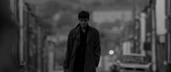 Movie still from “Control” (2007), directed by Anton Corbijn – A man in a trench coat standing on the street; Medium shot, Over the shoulder angle