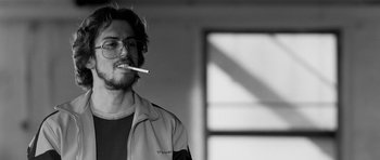 Movie still from “Control” (2007), directed by Anton Corbijn – A man with glasses is holding a cigarette in his mouth; Close Up shot, Low angle
