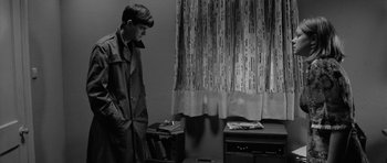 Movie still from “Control” (2007), directed by Anton Corbijn – A man in a trench coat standing next to a desk; Medium shot, Over the shoulder angle