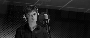Movie still from “Control” (2007), directed by Anton Corbijn – A young man wearing headphones and standing in front of a microphone in a recording studio; Close Up shot, Low angle