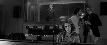 Movie still from “Control” (2007), directed by Anton Corbijn – A black - and - white photo of a man in a recording studio; Medium shot, Over the shoulder angle