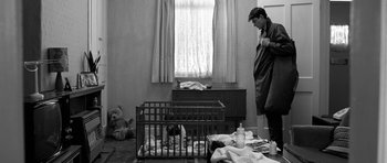 Movie still from “Control” (2007), directed by Anton Corbijn – A black and white photo of a man looking at a cat in a cage; Medium shot, Low angle