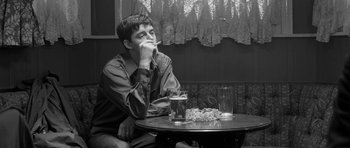 Movie still from “Control” (2007), directed by Anton Corbijn – A man sitting at a table with a cigarette in his mouth; Medium shot, High angle