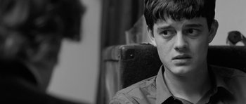 Movie still from “Control” (2007), directed by Anton Corbijn – A man sitting in a chair with a suit case in front of him; Close Up shot, Over the shoulder angle