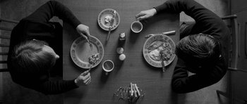 Movie still from “Control” (2007), directed by Anton Corbijn – A group of people sitting at a table with plates of food on it; Medium shot, Overhead angle