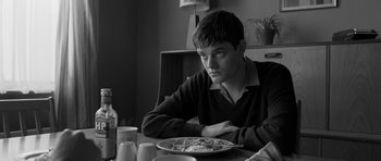 Movie still from “Control” (2007), directed by Anton Corbijn – A man sitting at a table with a plate of food in front of him; Close Up shot, Over the shoulder angle